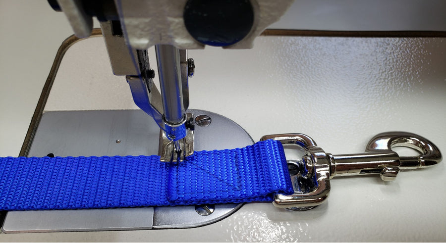 Blue webbing with a snap bolt being assembled using a box stitch on an industrial sewing machine.