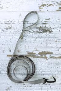 A long, gray nylon dog leash with an auto locking carabiner and loop handle, laid out on a white wood surface.