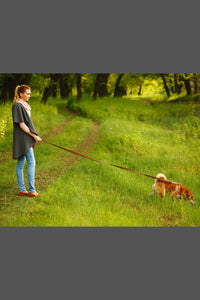 A woman in a grey sweater and jeans with her brown fluffy dog on a ten foot leash.