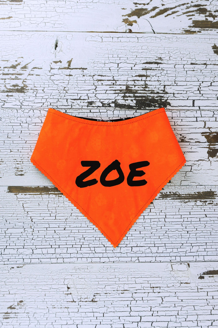 Personalize your reflective bandana with text up to 16 characters. Image shows the name Zoe in black on an orange bandana.