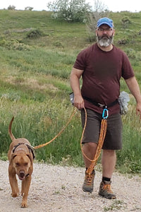 Rowan and his human returning from a trail hike, Rowan is on an adjustable long line that his human is using a hands free leash belt with.