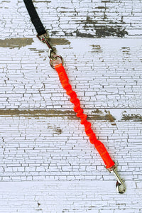 A 12 inch bungee leash add on is shown in neon orange, with a swivel snap bolt at the dog end, a black leash is connected to the heavy duty o ring at the opposite end.
