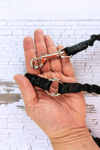 closeup of the bungee leash coupler hardware in the palm of an adult hand, includes a swivel snap bolt and a three quarters inch heavy duty welded o ring connecting the two bungee segments.