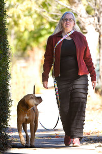 The shop owner is walking down the sidewalk wearing a cross body strap and leash connected to her dog Rowan walking at her side, looking up at her in hopes of getting a treat.