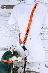 The do not pet in orange is shown here in a dog on right configuration with a d ring hardware selection, positioned on a mannequin with a dog mannequin by the side.