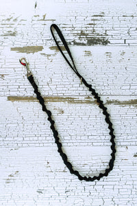 Handheld bungee leash shown in black webbing in a flat lay with a swivel snap bolt at one end and a loop handle at the opposite end.