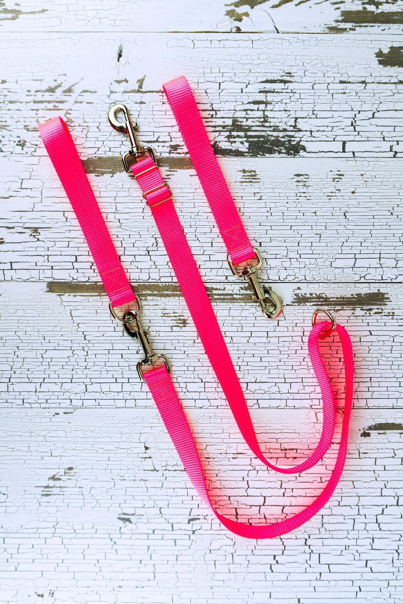 Adjustable no pull leash is shown in neon pink in a flat lay with both the leash handle with the swivel snap bolt and the leash handle with a d ring that converts the leash to a standard handheld leash.