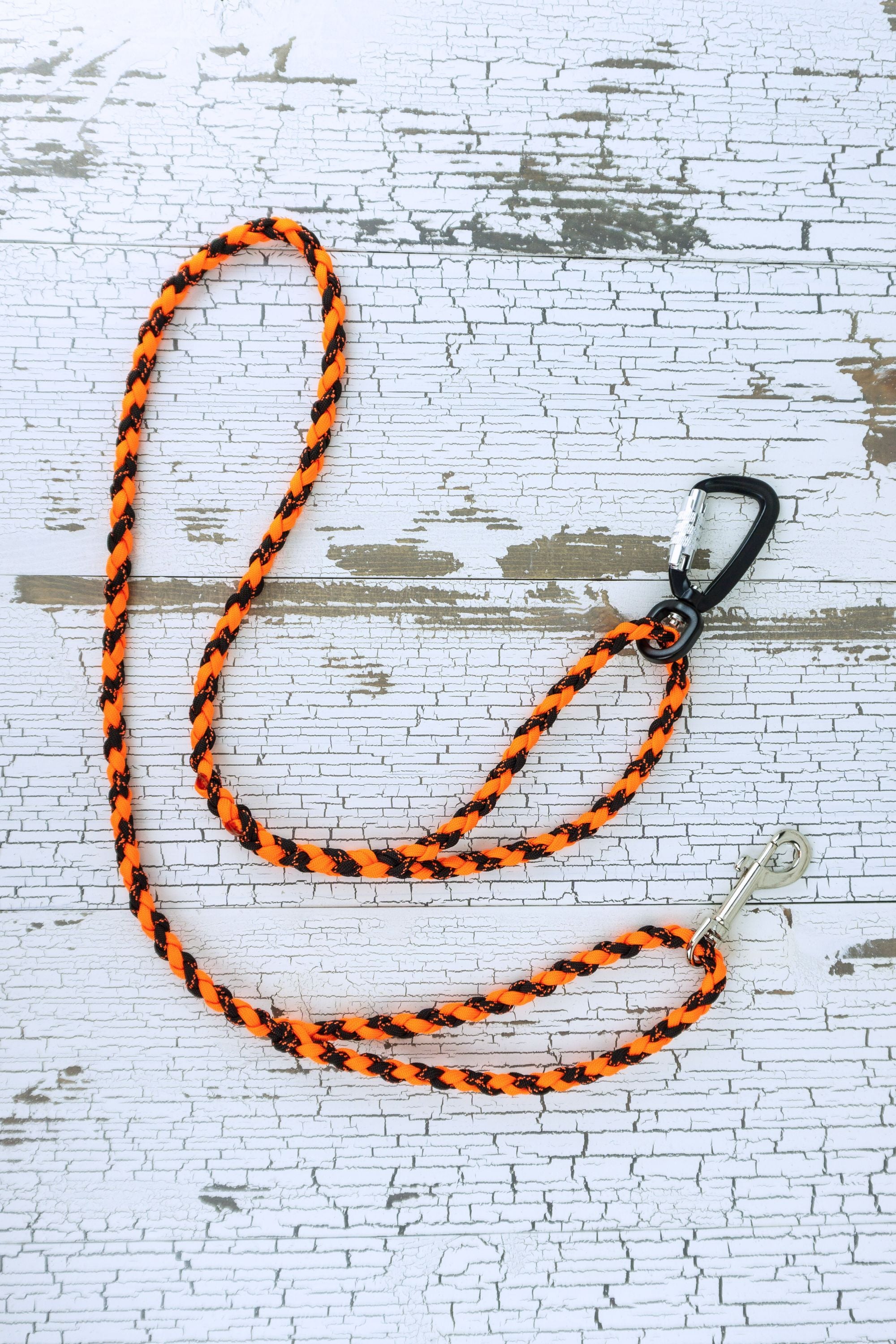 Neon orange and black braided paracord leash in a flat lay, showing loop handles at each end with a auto locking carabiner at one end and a swivel snap bolt at the other end.