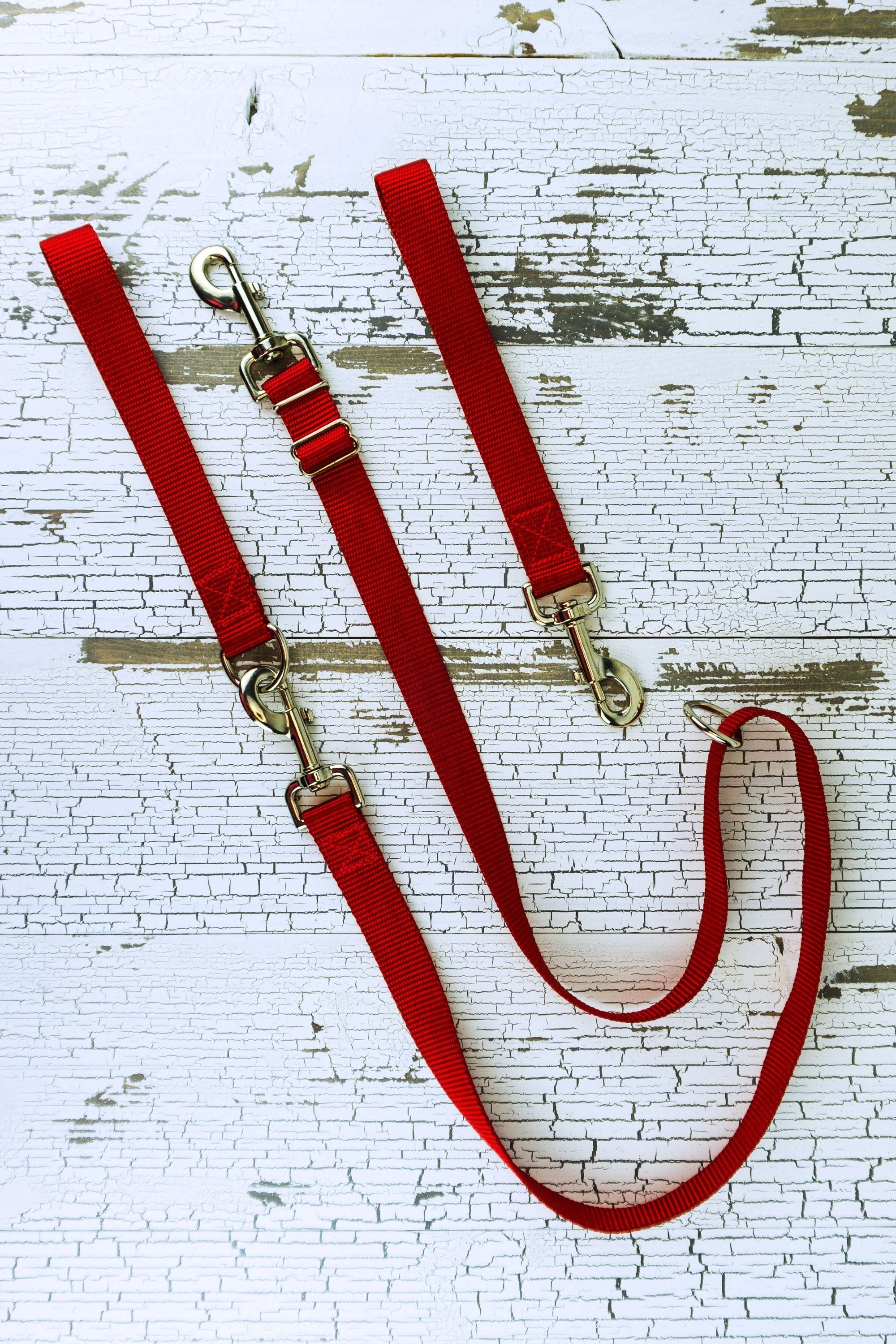 Adjustable no pull leash is shown in red in a flat lay with both the leash handle with the swivel snap bolt and the leash handle with a d ring that converts the leash to a standard handheld leash.